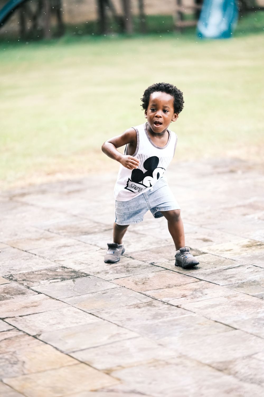 Young child in Mickey Mouse shirt runs playfully on outdoor patio.