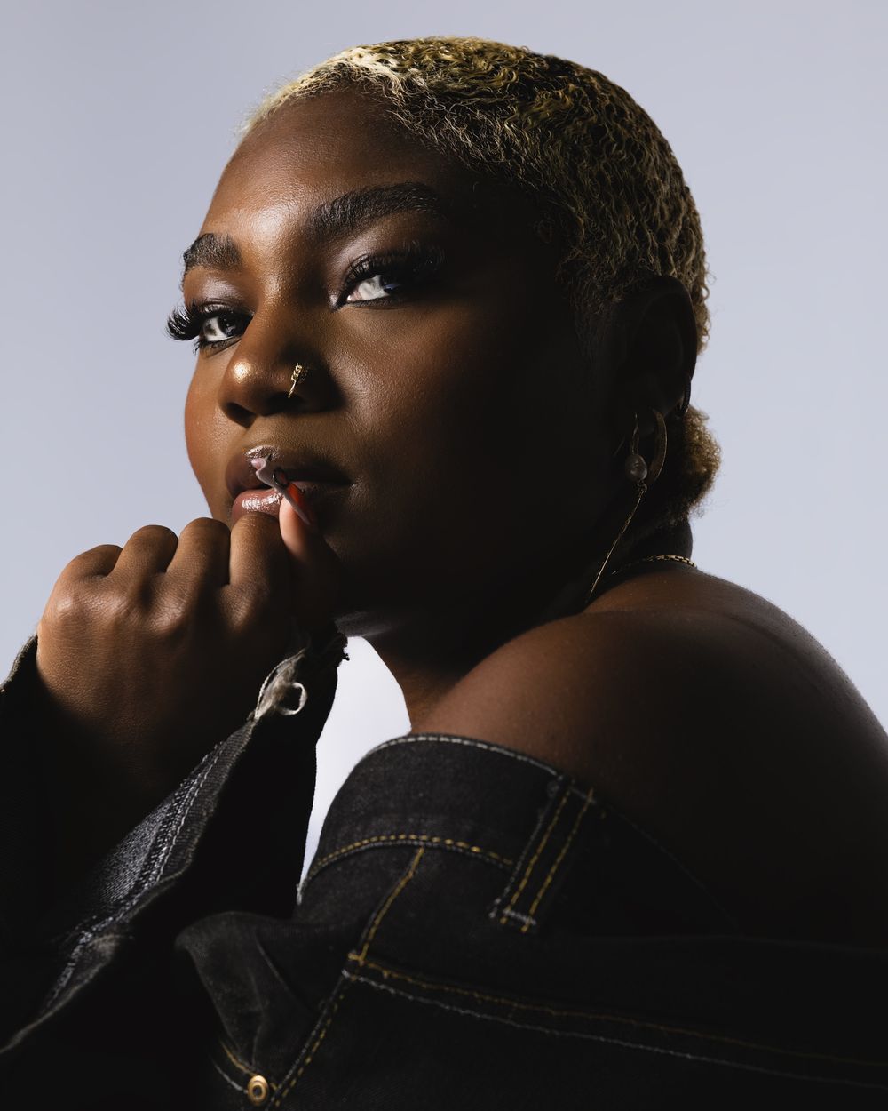 Artistic portrait shot with soft lighting highlighting a denim jacket against a dark background.