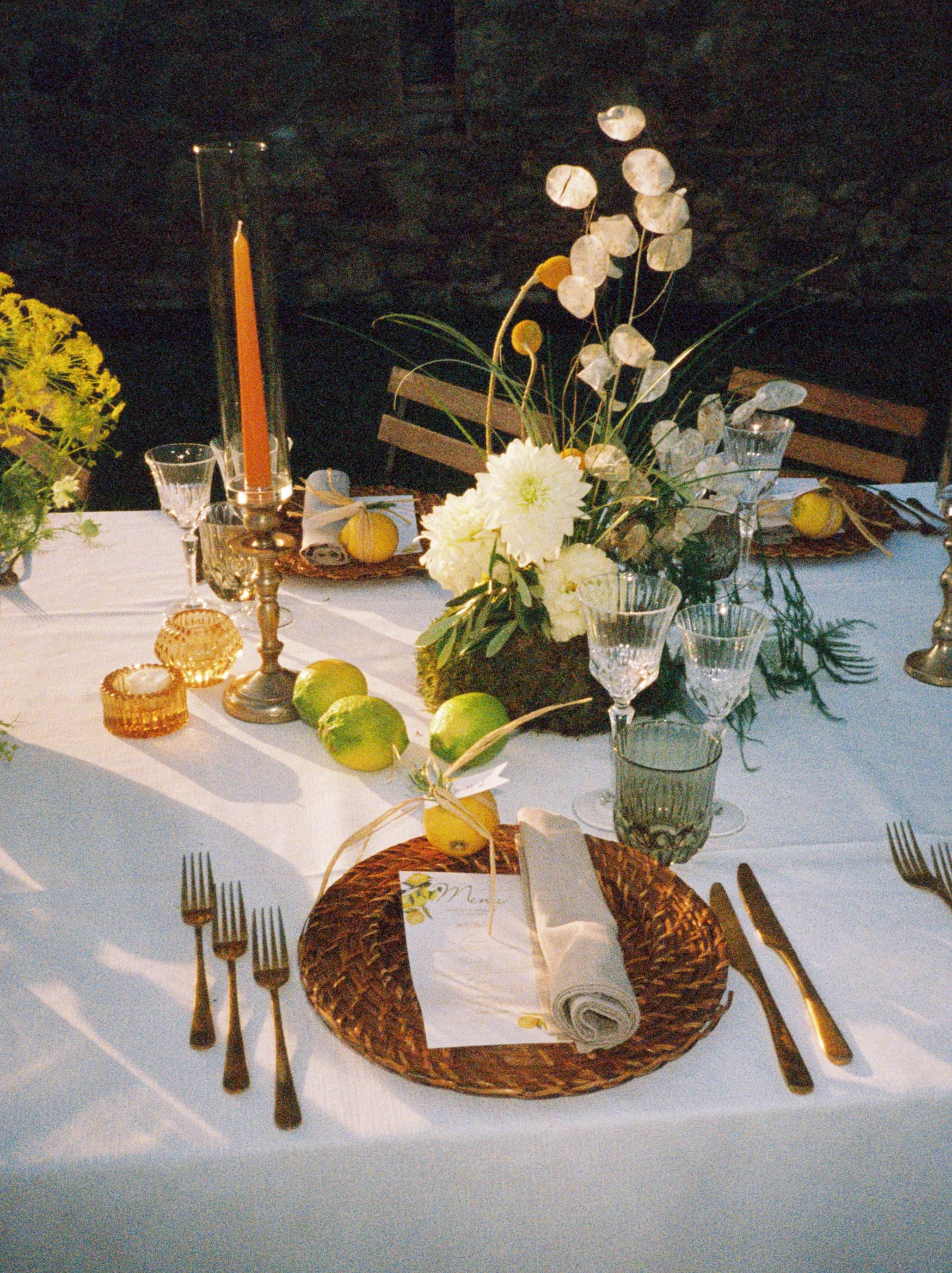 Elegant table settings with woven charger plates, glassware, and delicate white floral centerpieces on a crisp white tablecloth.