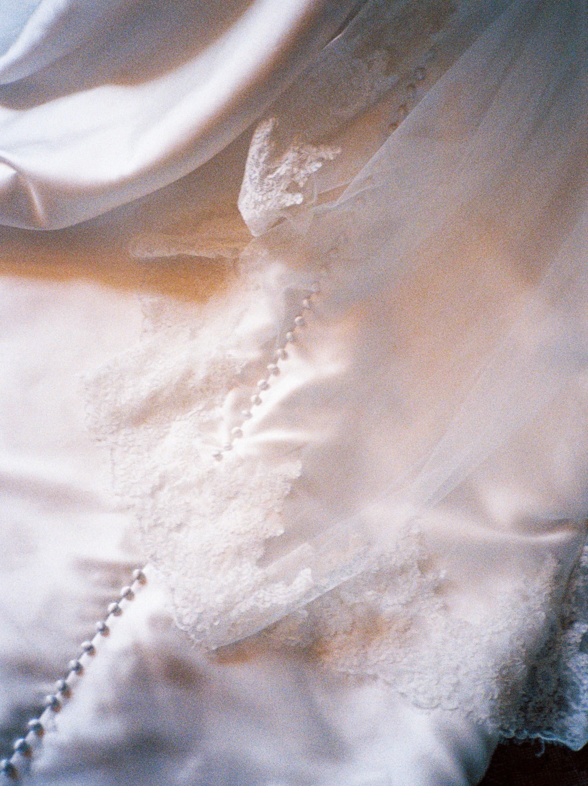 Close-up detail of delicate white lace and beading on a wedding dress fabric.