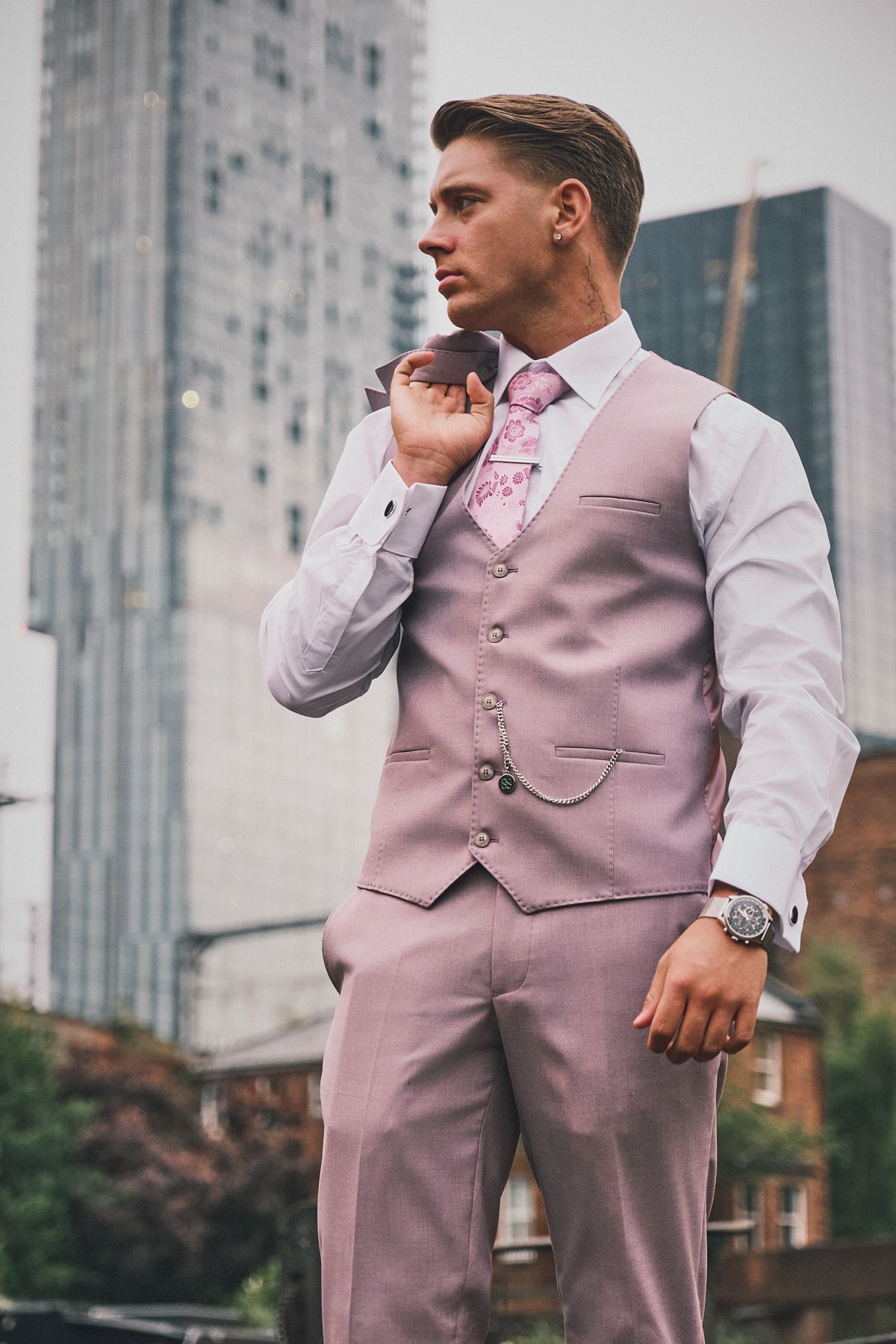 Model in pink suit vest and tie, posing outdoors in urban setting, ideal for lifestyle menswear photography