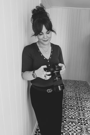 Person in black clothing holding a camera while taking photos on a decorative tiled floor.