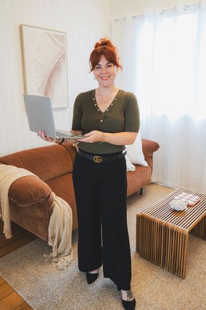 A person wearing a dark green top and black pants stands in a living room with a brown couch and wooden bench.