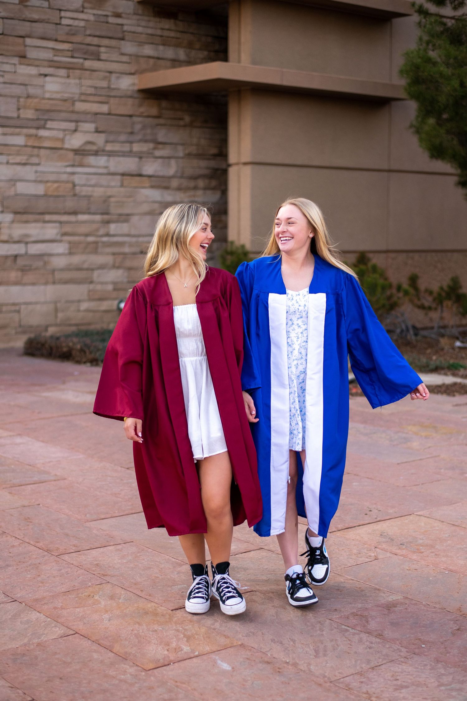 Two friends laughing together wearing graduation robes in burgundy and blue.