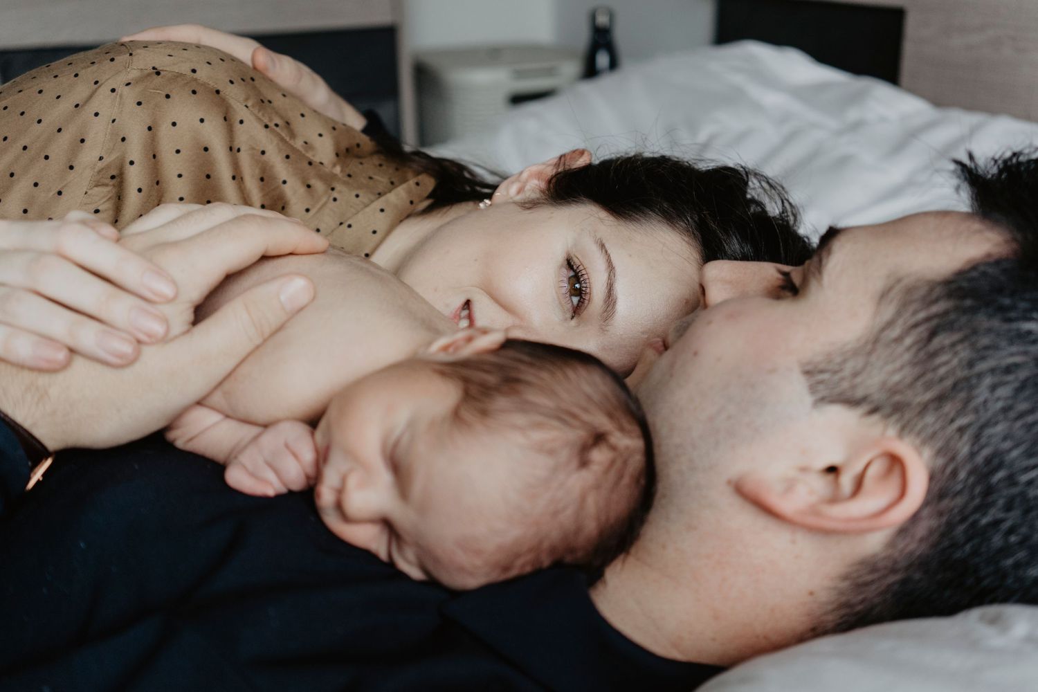Família acolhedora deitada na cama com o bebê recém-nascido adormecido entre os pais, transmitindo amor, intimidade e o vínculo especial dos