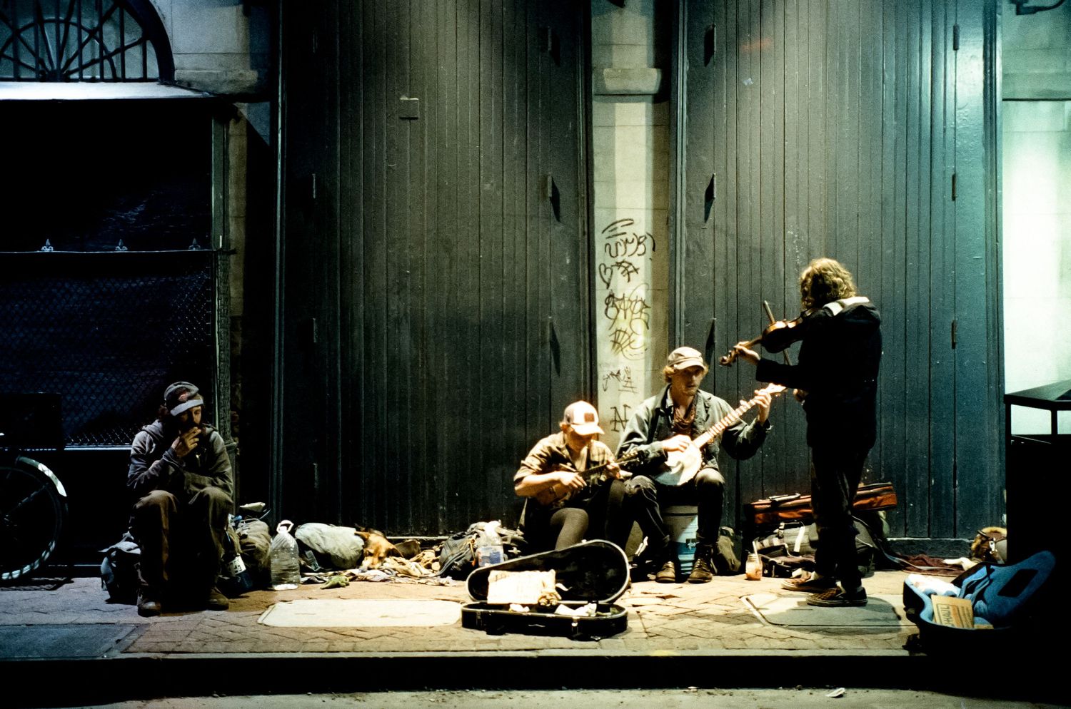 Musicians performing on the street with instruments and equipment in a dimly lit urban setting.