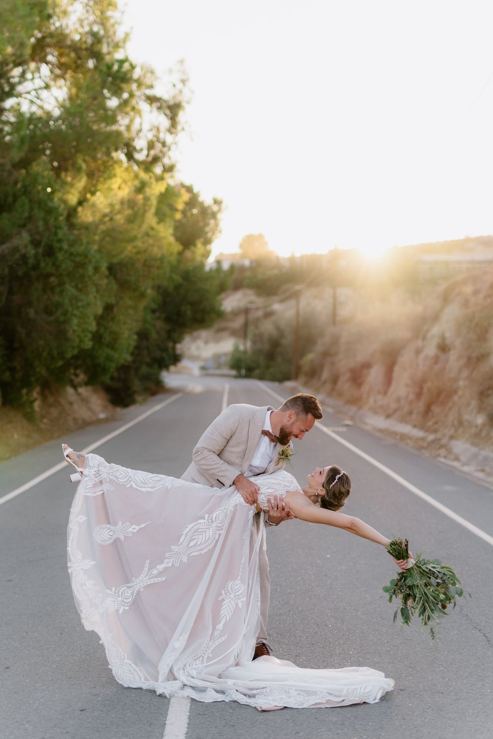 Romantic sunset dip pose on empty road with flowing white wedding dress.