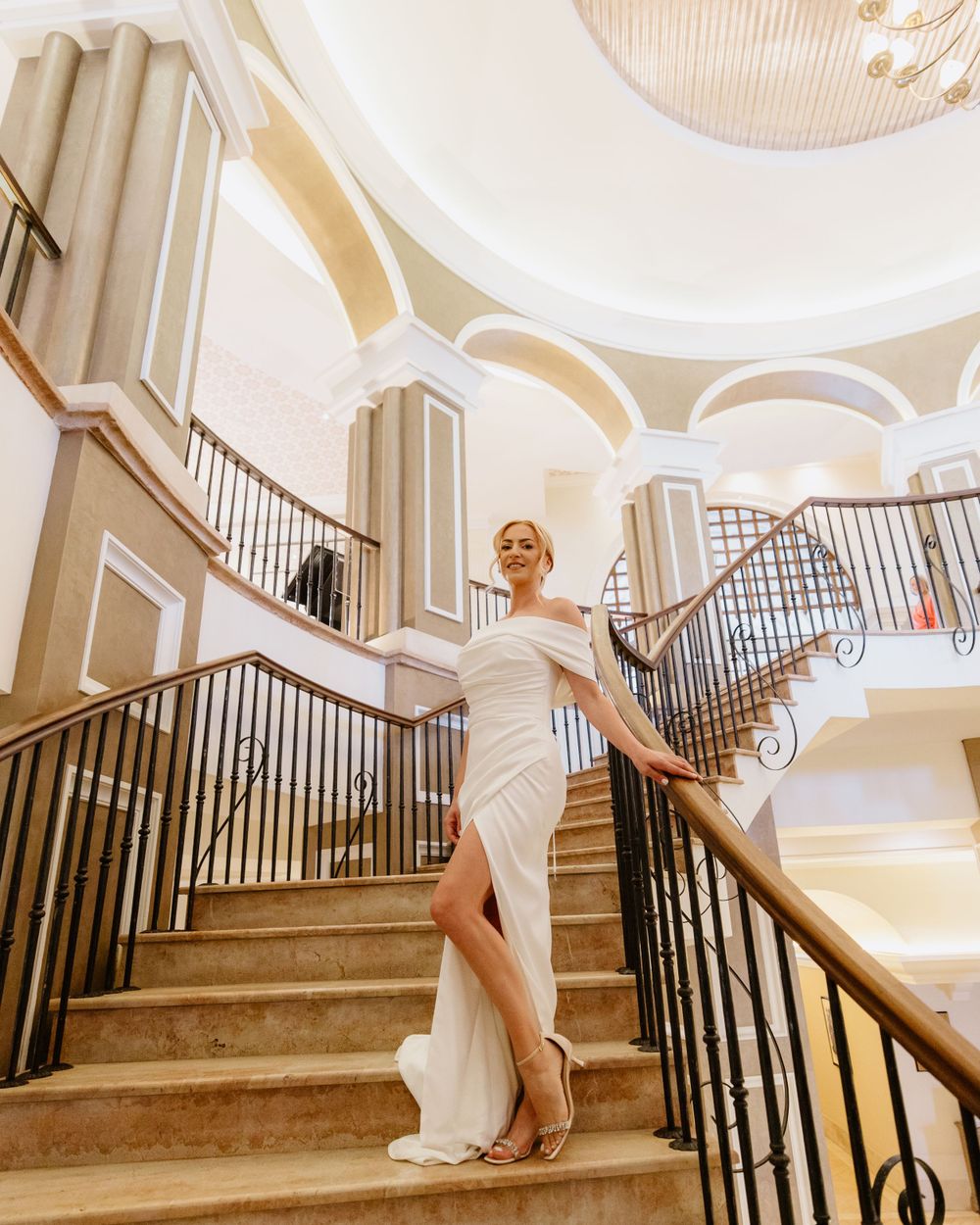 Elegant bride poses on the grand staircase of Elysium Hotel in Paphos, radiating style and confidence in a luxurious setting.