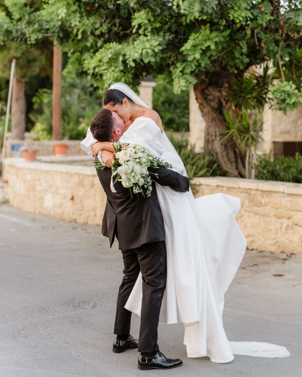 Loving embrace between newlyweds on stone pathway surrounded by greenery.