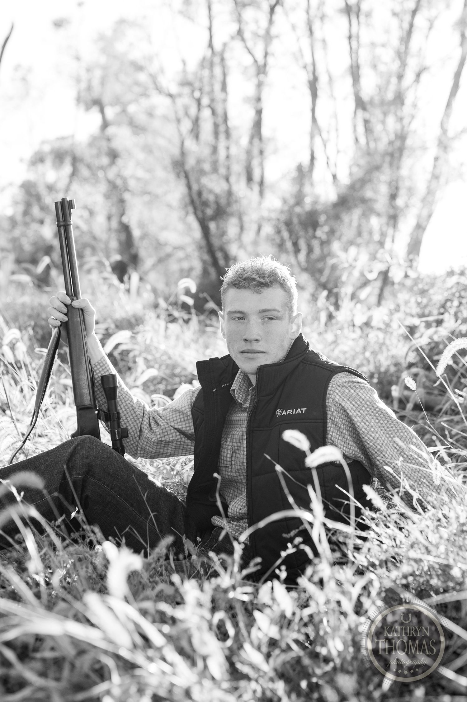 Black and white portrait of someone with rifle in tall grass.