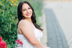 Portrait of a person in a white dress standing outdoors surrounded by lush greenery and blooming flowers.