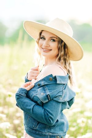 Stylish portrait of someone wearing a wide-brim hat and denim jacket in a sunlit meadow with wildflowers.
