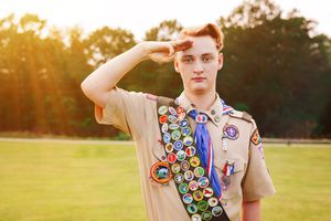 Scouts in uniform stand at salute against a golden sunset in a grassy field during an outdoor ceremony.
