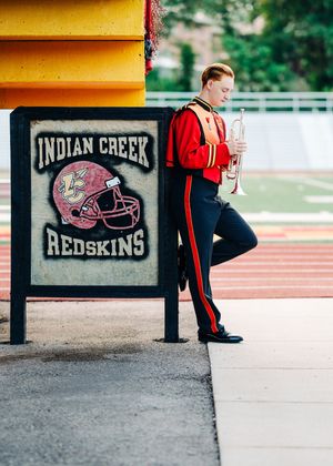 High school athlete stretches before practice at Indian Creek field with sports signage visible in the foreground.