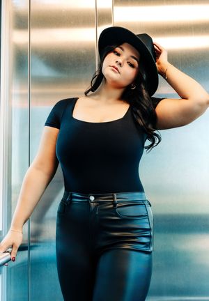 Plus size model in black outfit strikes elegant poses against modern interior backdrop with soft lighting.