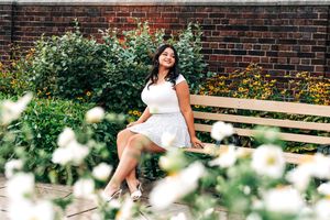 Woman in white dress relaxes on wooden bench surrounded by blooming daisies in garden setting.