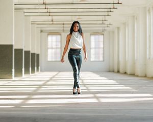 A lone figure walks down a sunlit industrial corridor with dramatic shadows cast through multiple windows.