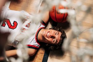 Smiling basketball player lying on court floor viewed through net, wearing red and white jersey number 2, holding basketball.
