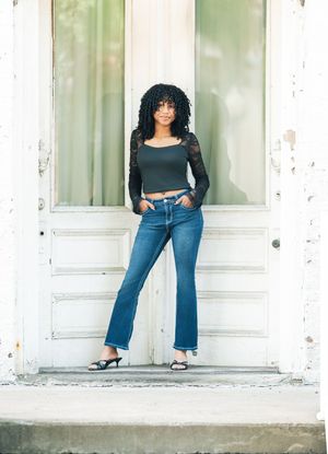 Young woman in flare jeans and dark crop top poses confidently in a white doorway outdoors.