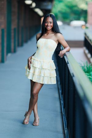 Model poses in an elegant off-shoulder ruffled white summer dress against an urban backdrop with iron railings.