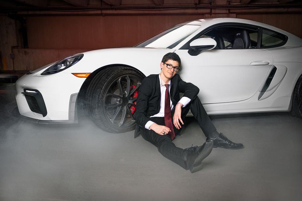 Luxury white Porsche sports car with someone posing next to it in a dark indoor setting.