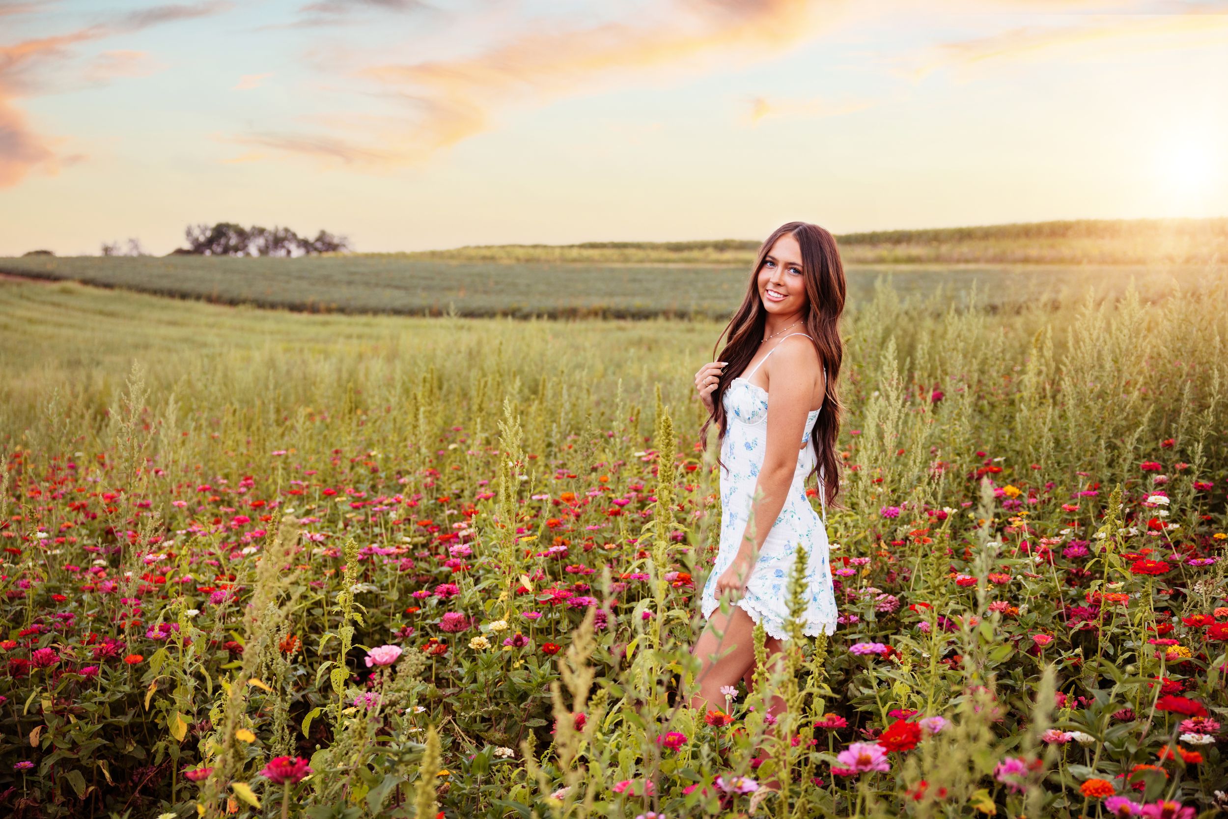 A white dress stands out against a field of red wildflowers during golden hour sunset.