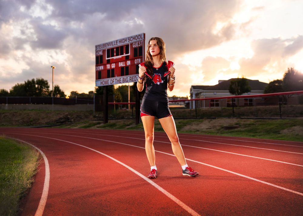 Runner on track at sunset with scoreboard in background creating dramatic sports portrait.
