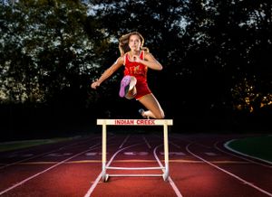 Track athlete clearing hurdle on running track at dusk with dynamic form and red uniform.