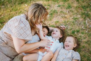 A loving moment shared between a parent and children laying in grass during a playful outdoor photo session.