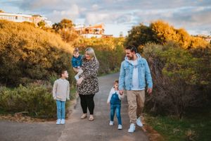 A family takes an autumn walk together on a dirt path with golden sunlight and houses on a hill in the background.