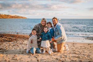 A family enjoys quality time together on a sandy beach at sunset with ocean waves and cliffs in the background.
