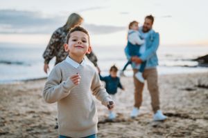 Family enjoying a playful moment together on a beach at sunset while walking along the shoreline.