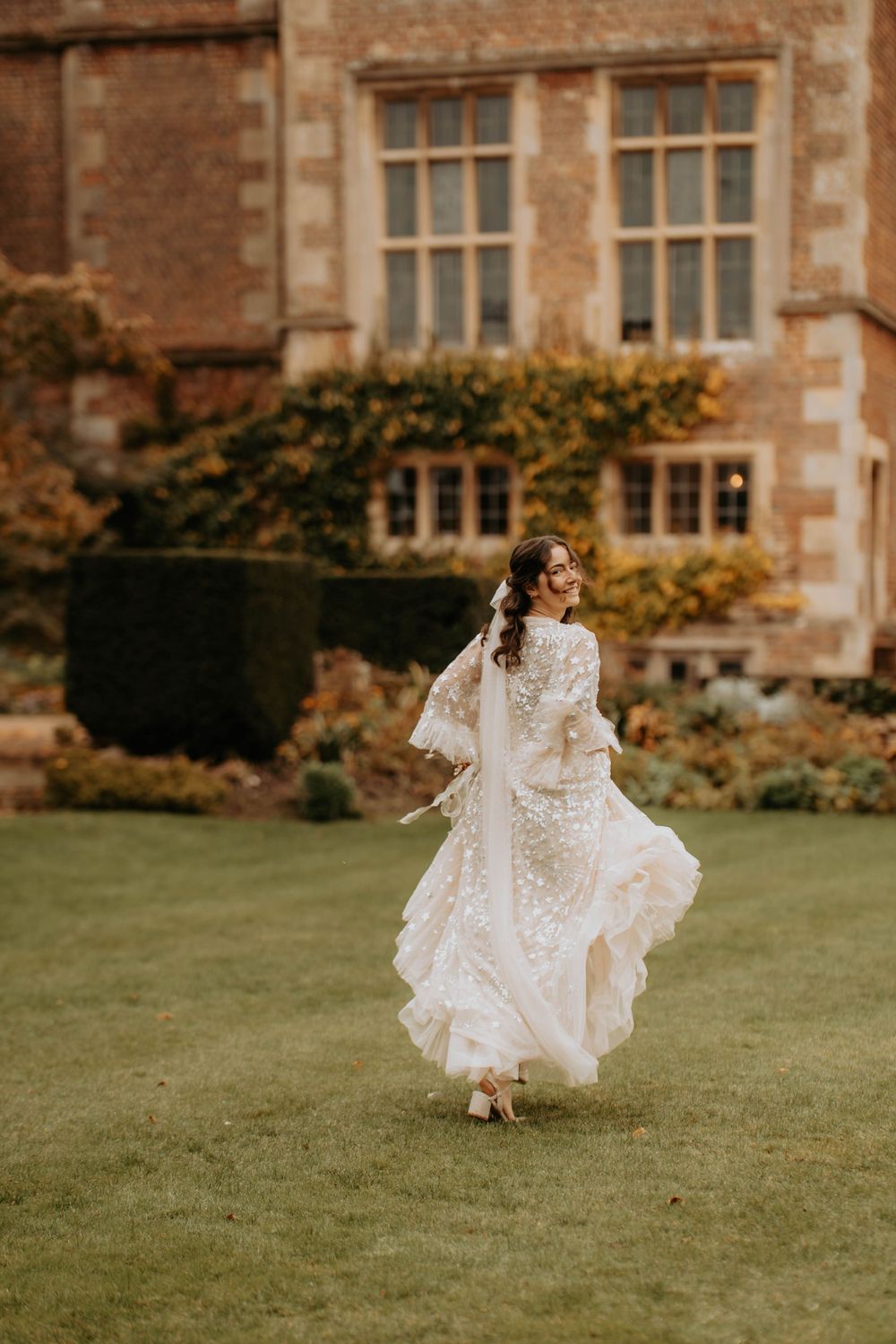 A bride in a flowing white dress runs across a castle lawn with historic architecture in the background.