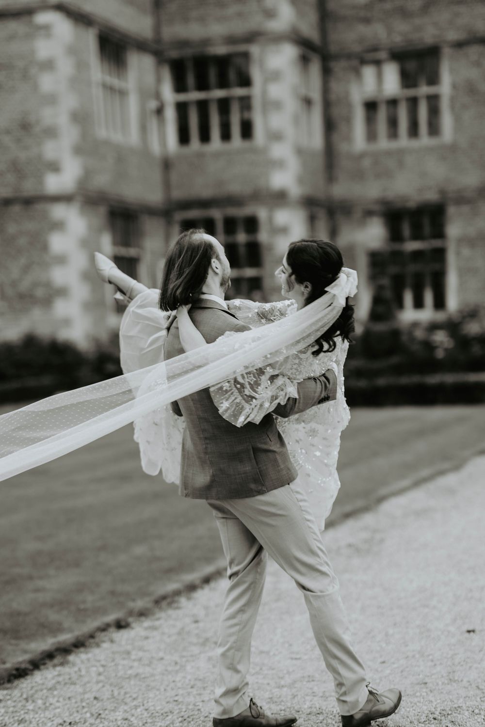 A couple spins and dances together on a stone path in front of a historic building in black and white.