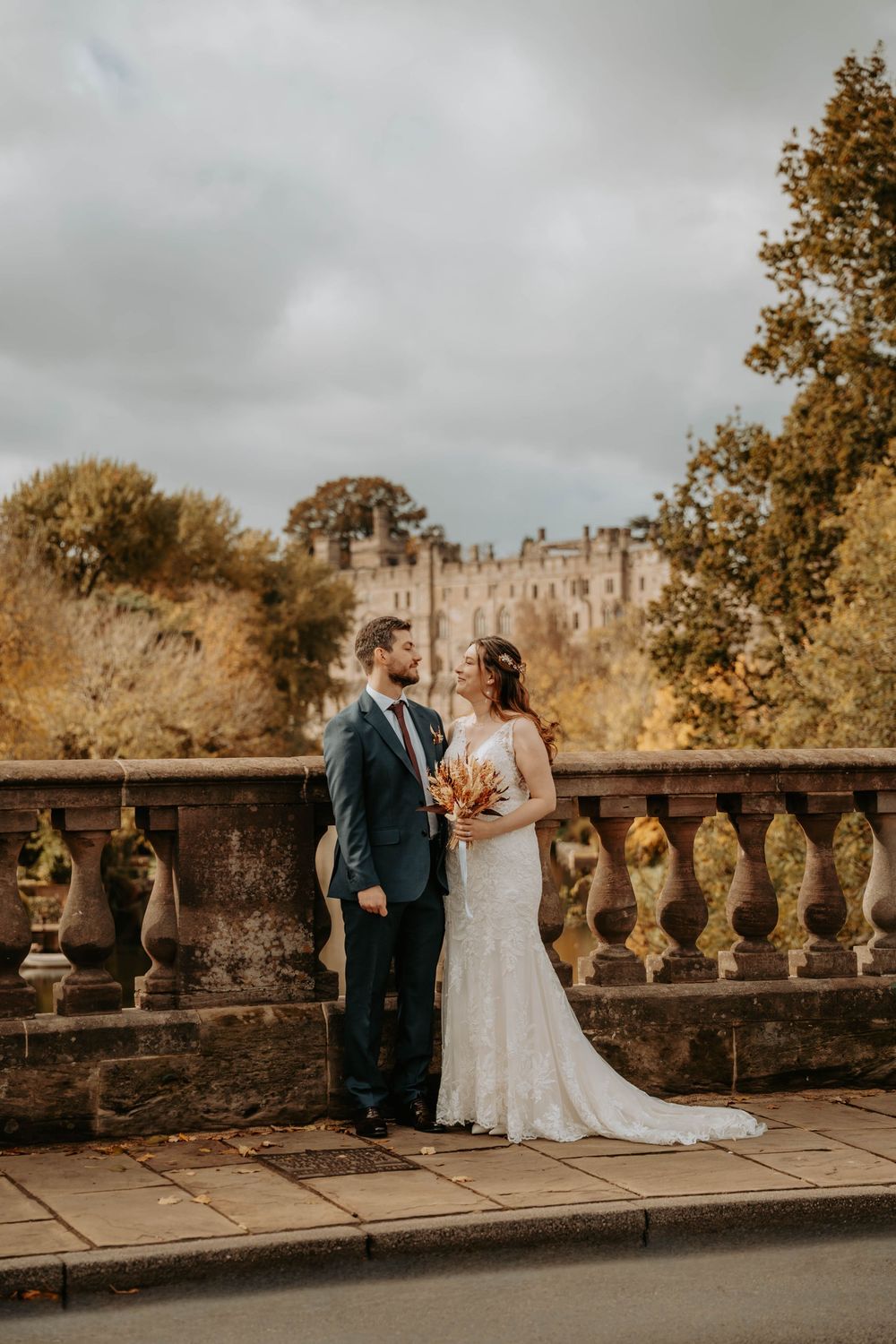 A romantic wedding couple shares intimate moments along a stone balustrade at a historic castle venue.