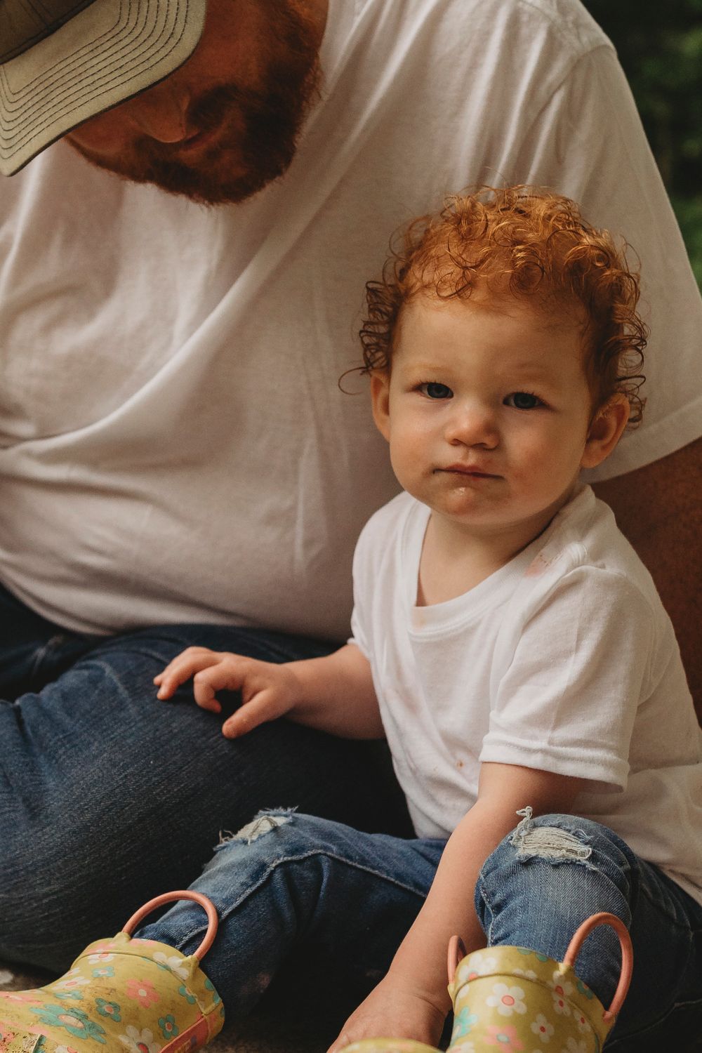 Child wearing white t-shirt and jeans sitting outdoors.