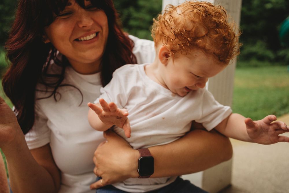A candid moment of joyful laughter and play between parent and child in white shirts against a green background.