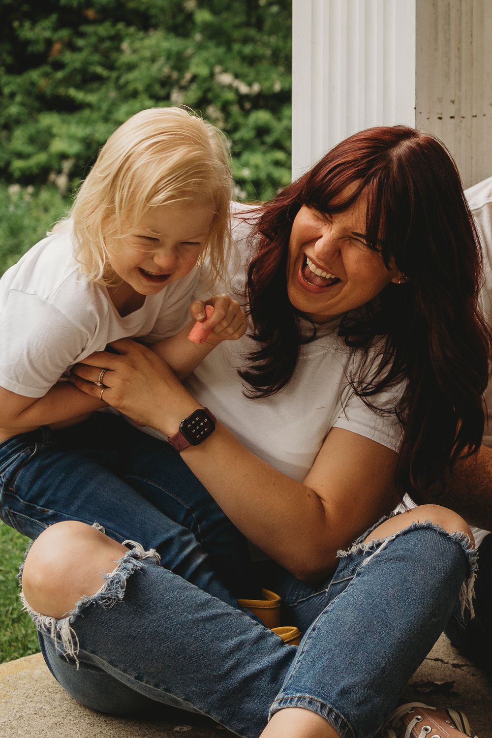 Two people share an authentic moment of laughter while sitting on outdoor steps in casual denim.
