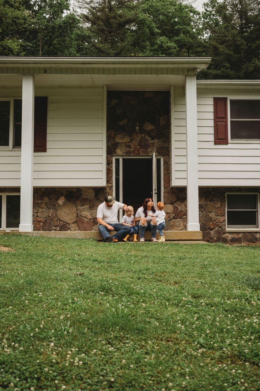 Family sitting together on front porch steps of white house with stone foundation.