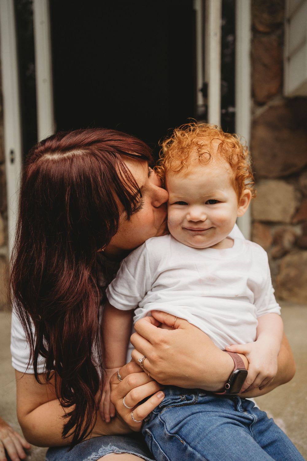 Tender moment captured as parent gives child a loving kiss on white house porch.