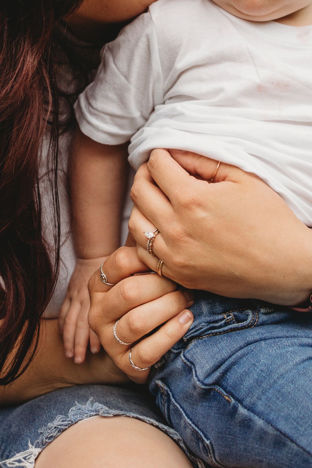 Close-up of hands wearing multiple delicate rings holding onto white fabric and denim.