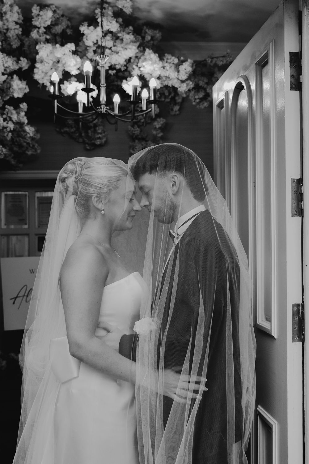 An intimate black and white portrait under crystal chandeliers with delicate veil details.