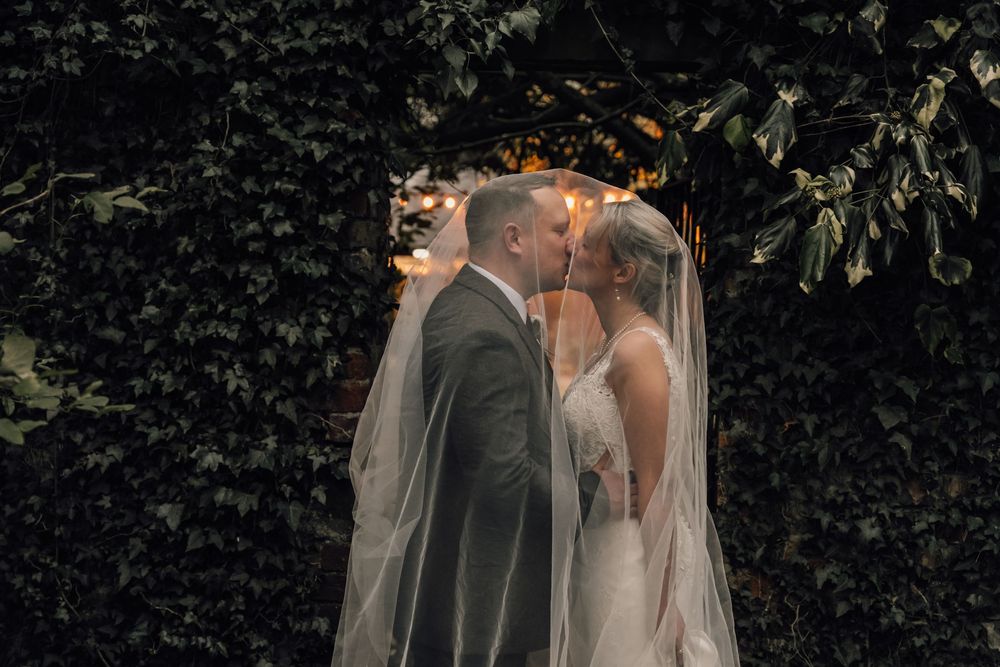 Wedding couple sharing intimate moments through a sheer veil in dark outdoor setting.