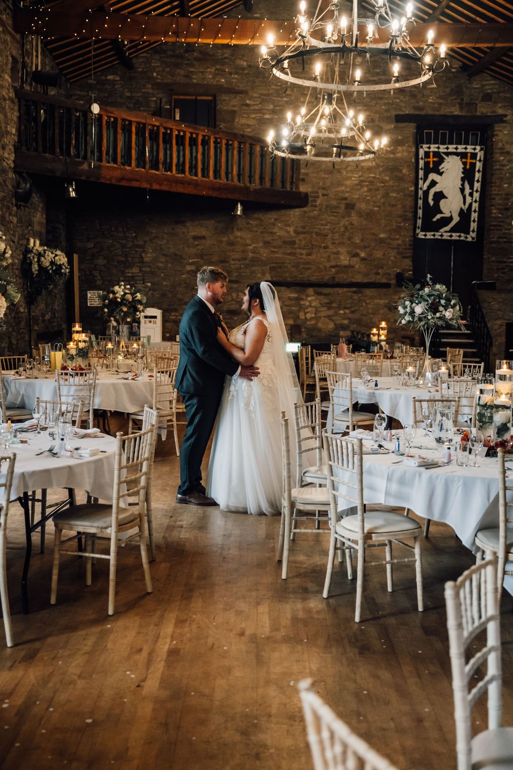 Rustic barn wedding reception venue with elegant white table settings and chandelier lighting.