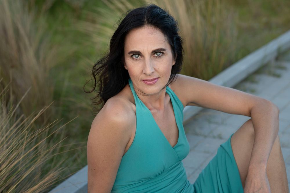 Elegant woman in teal halter dress sitting outdoors among ornamental grasses.