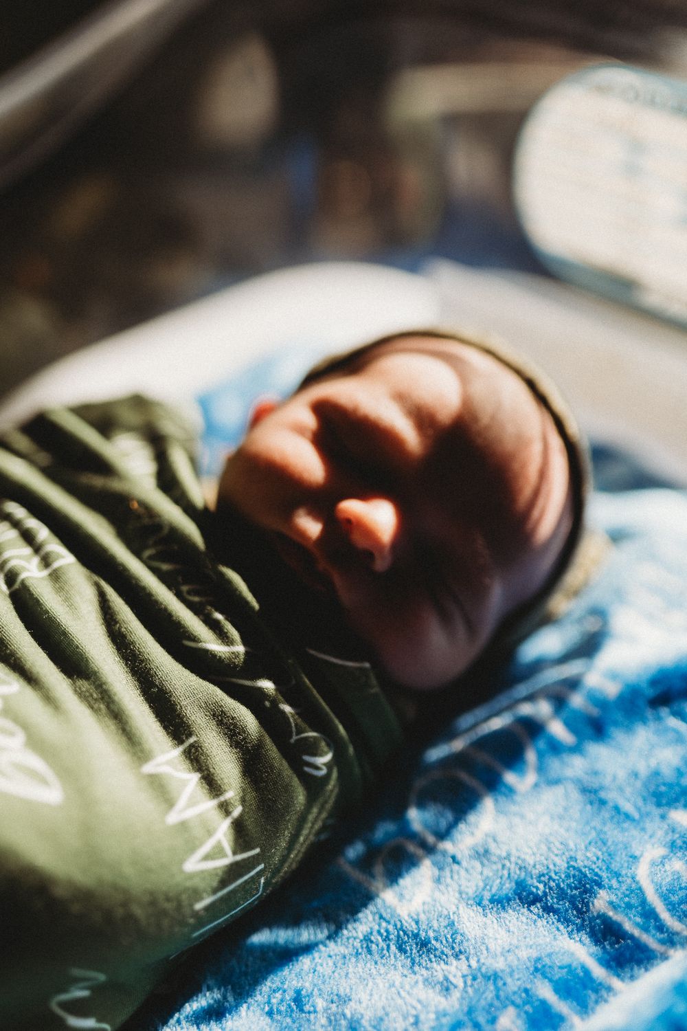 Newborn baby swaddled in a green blanket sleeping in soft natural window light.