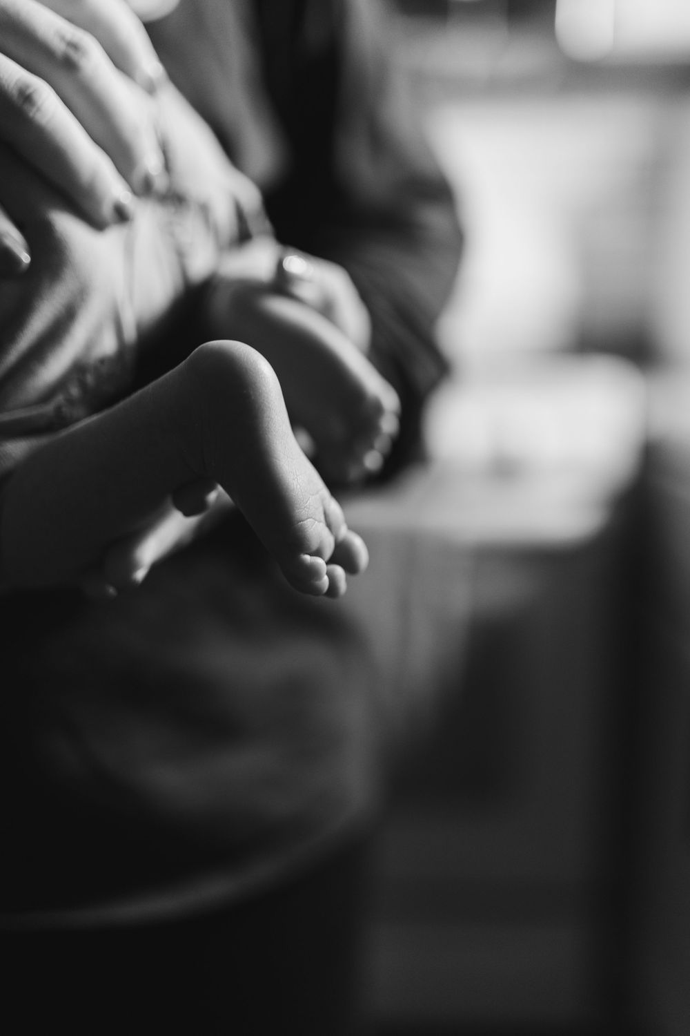 Black and white close-up of a newborn baby's tiny fingers resting in an adult's gentle hands.