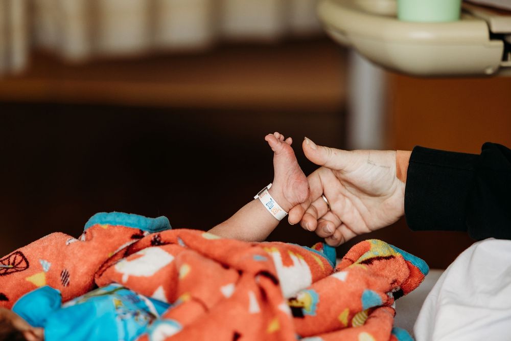 A parent gently holds a newborn baby's tiny feet with a hospital ID bracelet on a colorful blanket.