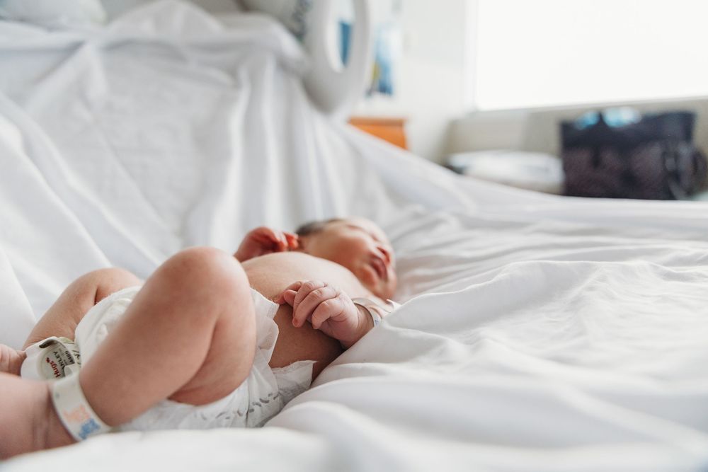Newborn baby lying on white hospital bed sheets wearing a diaper after birth.