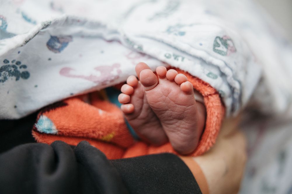 Close-up of tiny newborn baby feet wrapped in a soft orange towel and white patterned blanket.